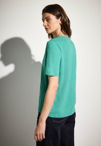 Mintgrön t-shirt med kort ärm i textilstruktur, med rak passform och avslutade fållar, kombinerad med mörka jeans.