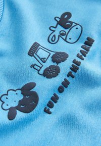 Lichtblauwe katoenen shirt met zwarte rubberen boerderijthema afbeeldingen: een schaap, een koe en een tractor met de tekst "PLEZIER OP DE BOERDERIJ."