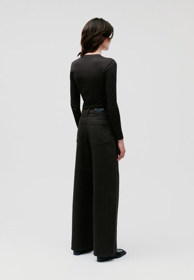 Top a maniche lunghe nera abbinato a pantaloni larghi grigio scuro. I pantaloni presentano un design con tasca posteriore e un sottile accento in pelle in vita.