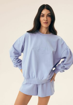 Jasnoniebieska bluza z ribbowym wykończeniem u dołu i przy mankietach, z tłoczonym napisem "West Virginia". W komplecie z pasującymi szortami.