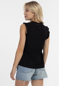Top nero senza maniche con spalline arricciate, caratterizzato da un dettaglio a chiave sulla schiena e un tessuto testurizzato. Abbinato a pantaloncini di jeans strappati.
