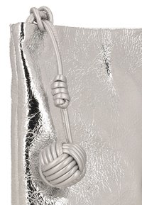 Metaliczna srebrna torba o pomarszczonej fakturze, z charakterystycznym wiązanym uchwytem. Materiał wydaje się być skórą syntetyczną.