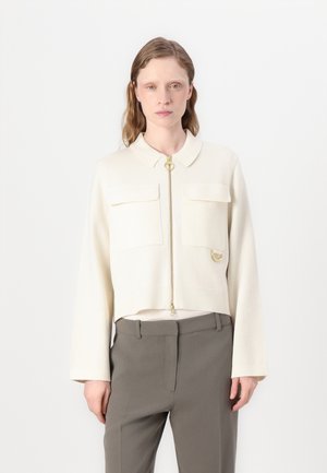 Crème-kleurige cropped jack met een kraag, voorzien van een rits aan de voorkant, twee borstzakken en gouden hardware accenten. Fluweelzachte stof.