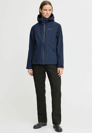 Navy waterproof jacket with a zip closure, adjustable hood, and two side pockets, paired with black pants and black footwear.