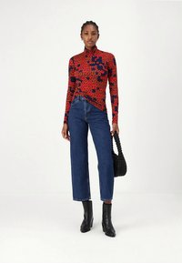 Ilgomis rankovėmis, raudonas golfas su juodu gėlių raštu, derinamas su aukštu liemeniu ir plačiomis mėlynomis džinsinėmis kelnėmis bei juodais kulniukais iki čiurnos.