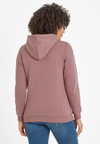 Raspberry-colored hoodie with textured fabric, long sleeves, and adjustable drawstring hood, worn over blue jeans.