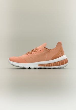 Chaussure de sport en maille corail clair avec fermeture à lacets à l’avant, semelle blanche rembourrée et détail texturé au talon sur fond neutre.
