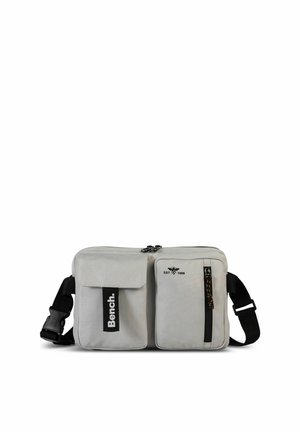Graue Stoff-Umhängetasche mit zwei Fronttaschen, Reißverschluss, verstellbarem Riemen und Bench-Logo; besitzt ein schlankes rechteckiges Design.