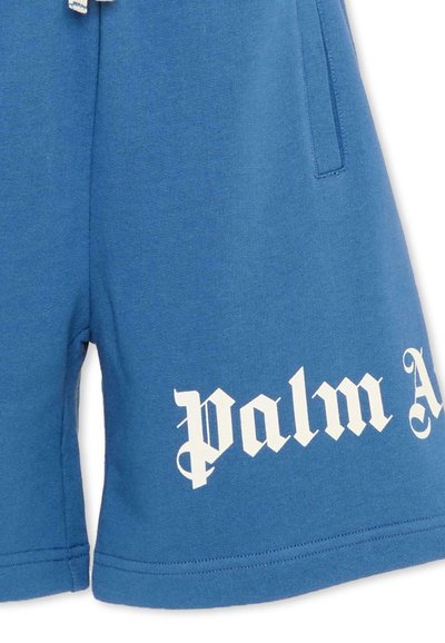 Shorts en coton bleu avec cordon blanc et texte "palm A" de style gothique imprimé en blanc sur la partie inférieure de la jambe droite.