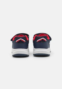 Scarpe sportive navy con accenti in rete rossa, una suola bianca curvata e cinturini in velcro; presentano materiali texturizzati e elementi di design a strati.