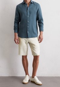 Ljusblå linne skjorta med knappar och krage, i kombination med krämfärgade linne shorts och vita sneakers med beige sula.