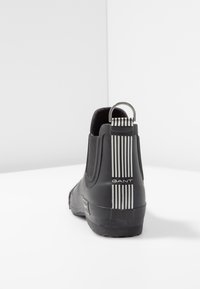 Zwarte rubberen Chelsea-boot met elastische zijkanten, voorzien van een gestreepte lus en logodetail. Gladde textuur met een platte zool.