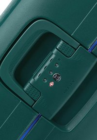 Poignée de valise rigide verte avec une prise texturée, serrure à combinaison intégrée et marque Delsey. Fini lisse avec accent bleu.