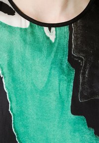 Tela con patrón abstracto en negro y verde, de textura suave. Escote redondeado en negro con un ligero brillo. El diseño presenta formas fluidas que parecen pinceladas.