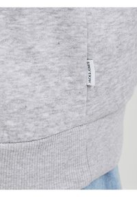 Šedý svetr s měkkou texturovanou látkou, žebrovaným lemem a malou značkou na boku s nápisem "JACK & JONES".