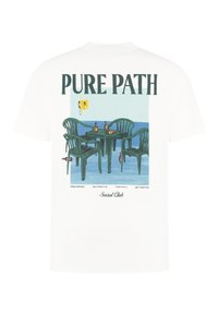 Witte katoenen t-shirt met een kleurrijk ontwerp van groene plastic stoelen en een tafel, met de tekst "PURE PATH" erboven en "Social Club" eronder.