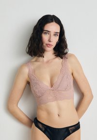 Krajkový bralet v jemne ružovej farbe s výstrihom do "V" a širokými ramienkami, doplnený čiernymi nohavičkami s krajkovým lemovaním a hladkým povrchom.