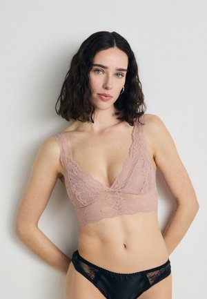 Lace bralette in soft pink with a v-neck design and wide straps, paired with black lace-trimmed panties featuring a smooth finish.