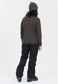 Brun långärmad topp med en texturerad yta, kombinerad med svarta vattentäta byxor och en grå stickad mössa. Svarta skor med detaljer.