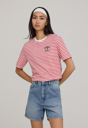 T-shirt a righe rosse e bianche con maniche corte, scollo rotondo e testo ricamato. Abbinata a pantaloni corti in denim blu a vita alta.