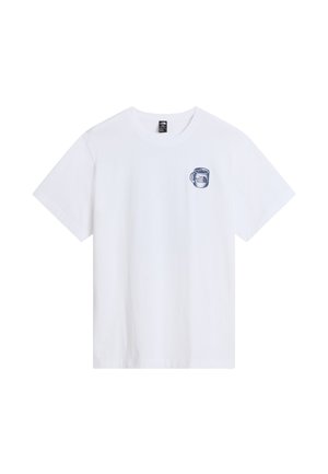 Personne portant un t-shirt blanc avec un dessin de camping-car préparant du café près des montagnes, avec le texte "Basecamp Barista" et le logo The North Face.