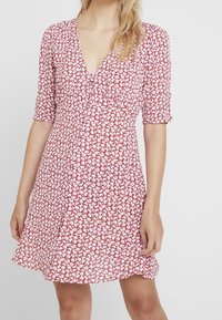 Rode bloemenjurk met korte mouwen, V-hals en een uitlopende snit. De stof heeft een klein wit bloemenpatroon over het geheel.