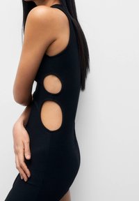 Robe noire à côtes avec découpes sur les côtés, sans manches et silhouette ajustée. Tissu doux et extensible.