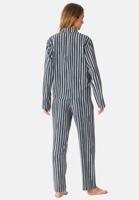 Gestreepte pyjama set in marineblauw en off-white, met lange mouwen en een relaxte fit. Materiaal lijkt zacht en soepel.