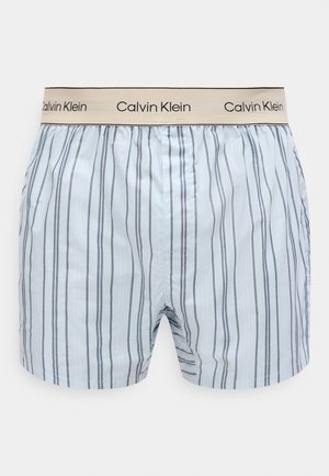 hele sinised bokserid vertikaalsete tumedate triipudega ja beež elastse vöökohaga, millel kordub "Calvin Klein" logo.