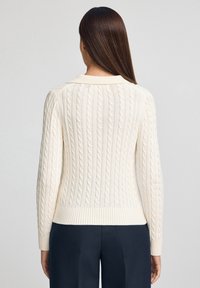Cremefarbener, grob gestrickter Pullover mit gerippten Bündchen und Saum, hoher Kragen und vertikalem Strukturmuster.