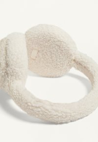 Cuffie in crema pelose realizzate in un tessuto testurizzato, con padiglioni arrotondati e una fascia elastica coordinata per calore e comfort.