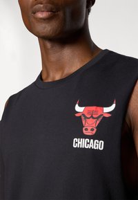 Črna brezramenska majica z rdečim logotipom Chicago Bulls, ki prikazuje bikovo glavo in besedo "CHICAGO" v beli barvi spodaj. Mehka tekstura tkanine.