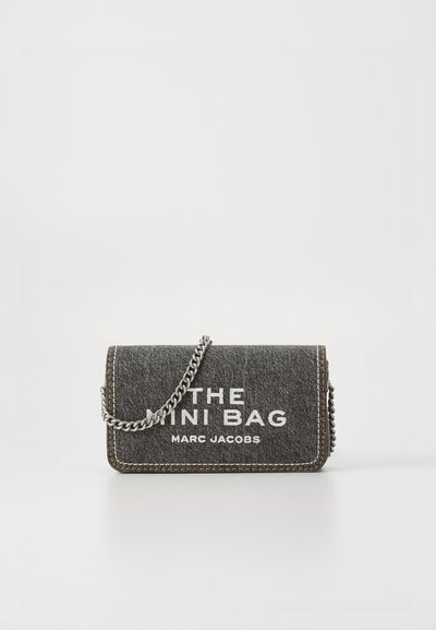 Geantă mini din țesătură gri închis cu text alb "THE MINI BAG MARC JACOBS" și o curea din lanț argintie, pe un fundal alb.