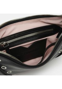 Interno di una borsa a mano in pelle nera con rivestimento rosa, dotato di una tasca con zip e di un compartimento aperto. Accenti in metallo visibili.