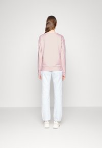 Felpa rosa chiaro con maniche lunghe, scollo arrotondato e polsini a coste, abbinata a pantaloni azzurri e sneakers bianche.