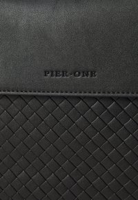 Sac à main tissé noir avec une surface texturée, arborant le logo embossé "PIER-ONE". Couche supérieure lisse avec un motif en diamant sur le corps.