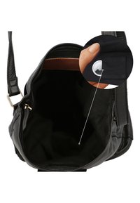 Borsa a mano in pelle nera con cerniera aperta che mostra l'interno vuoto e una mano che tiene una piccola tasca di stoffa contenente un dispositivo di tracciamento bianco.