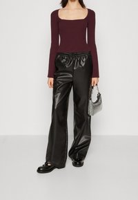 Bordowa prążkowana bluzka z długim rękawem i kwadratowym dekoltem, zestawiona z czarnymi szerokimi spodniami z imitacji skóry. Srebrna torebka na łańcuszku. Czarne buty.