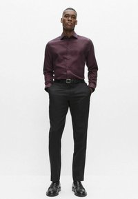 Bordeauxfarvet skjorte med lange ærmer og knapper, kombineret med sorte bukser og lædersko. Glat stof med klassisk krave og tætsiddende pasform.