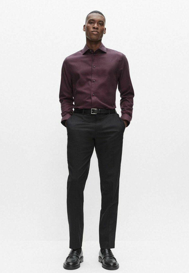 Bordeauxfarvet skjorte med lange ærmer og knapper, kombineret med sorte bukser og lædersko. Glat stof med klassisk krave og tætsiddende pasform.
