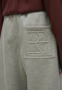 Hallid hallid dressipüksid tekstuuriga logo plakiga, millel on "R" ja "E". Kangas on pehme, elastne vöökoht ja küljetasku.