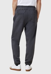 Grijze sweatpants met een elastische tailleband, twee achterzakken en een geborduurd onderste deel. Gepaarde met witte sneakers met bruine zolen.