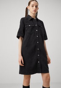 Svart denimskjortklänning med korta ärmar, knappslå framtill, två bröstfickor och rak form. Designad med en krage och sidofickor.