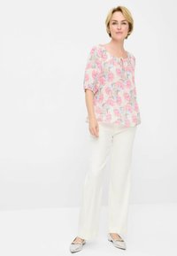 Korte mouwen, roze blouse met een bladerenprint, gecombineerd met witte wijde broek en zilveren instapschoenen.