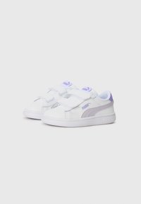 Baskets blanches avec accents violets, présentant un dessus en synthétique lisse, des sangles Velcro et une semelle en caoutchouc texturé. Logo PUMA inclus.