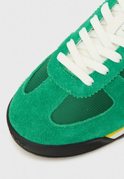 Zelené tenisky s nubukovým zvrškom, sieťovinou, bielymi šnúrkami a čiernou gumovou podrážkou. Na boku majú žlté a modré akcenty.