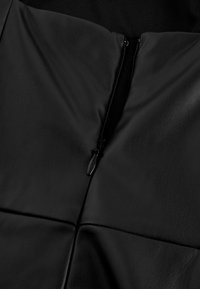 Vaatteet mustasta nahasta, jossa on vetoketjukiinnitys ja paneelimuotoilu. Sileä pinta, jossa on hienovarainen kiilto ja ompeluyksityiskohdat.