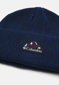 Bonnet en tricot côtelé bleu marine avec un patch logo représentant un design de montagne et le nom de la marque brodé dans une couleur contrastante.