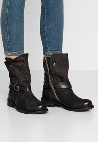 Bottines noires à tige en tissu texturé, dotées d'une fermeture éclair, de deux sangles en cuir et d'un talon bas.