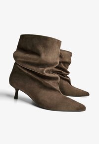 Stivaletti alla caviglia in camoscio marrone con design morbido e pieghettato, punte appuntite e tacco basso a gattino. La texture soffice valorizza l'estetica casual.